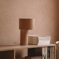 Minimalist beige lamp with a cylindrical base and a soft, rounded shade, set against a warm, muted backdrop.
