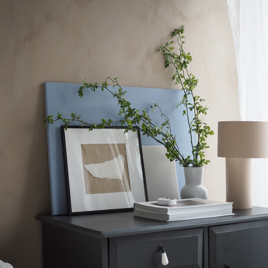 "Soft blue background with neutral tones, framed artwork, and greenery complementing a minimalist decor style."