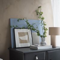 "Soft blue background with neutral tones, framed artwork, and greenery complementing a minimalist decor style."