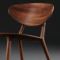 Wooden chair in rich walnut finish, featuring a smooth, curved seat and tapered legs against a dark background.