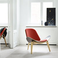 Hans Wegner Shell Chair in red upholstery with oak frame, set in minimal white interior with modern black artwork on windowsill.