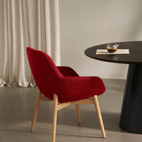 Red upholstered armchair with a sleek design, paired with a round dark table and soft beige curtains.