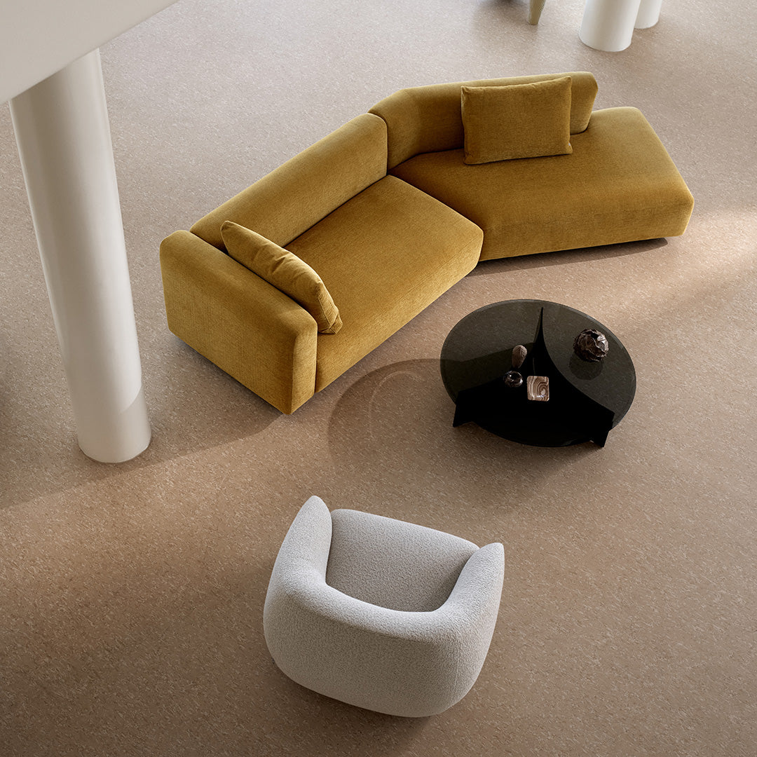 "Soft mustard yellow sectional couch with matching pillows, paired with a sleek black coffee table and white armchair."