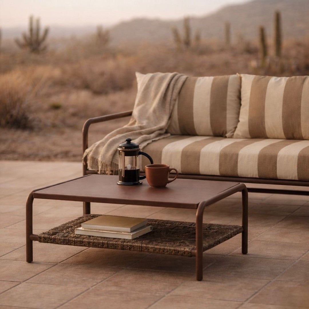 Brown and cream striped sofa with a minimalist coffee table and woven shelf, set against desert landscape.