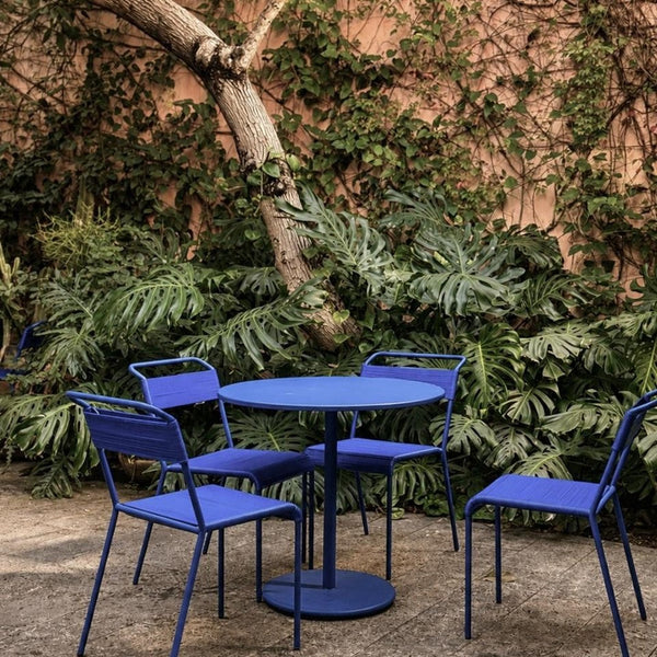 Vibrant blue round table and chairs, featuring a sleek design against a lush green backdrop. Perfect for outdoor settings.