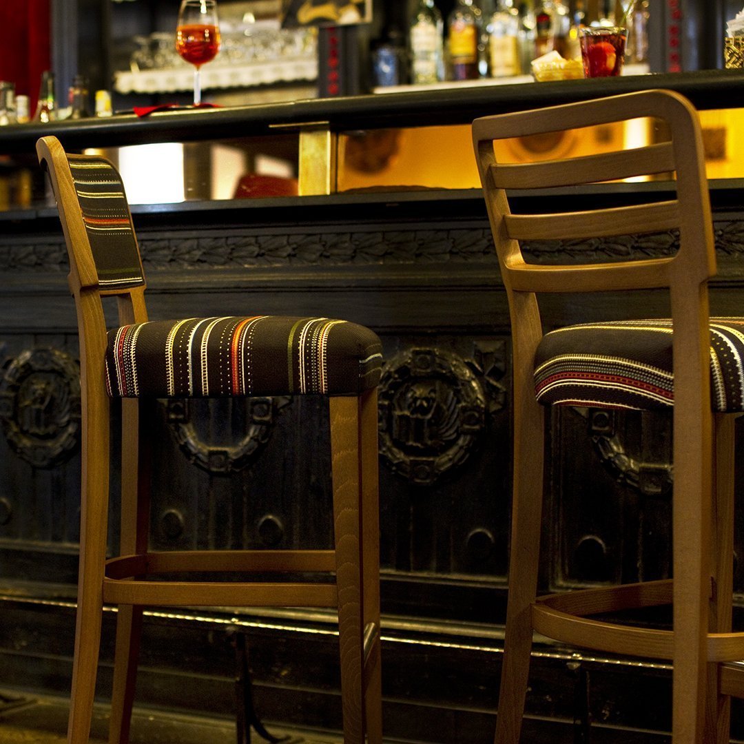 Striped bar stool cushions in warm earth tones, paired with natural wood frames in a rustic bar setting.