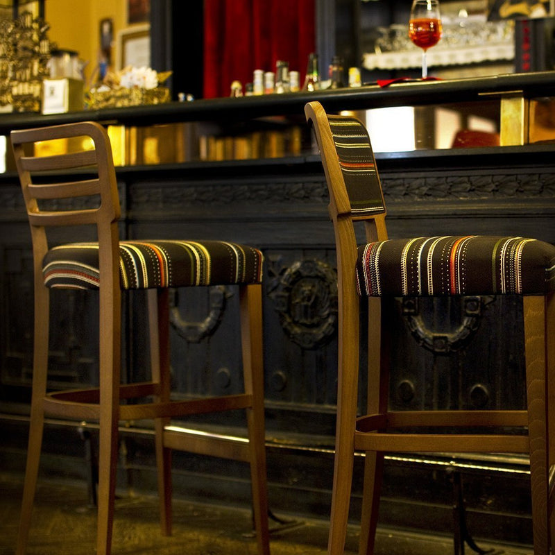 "Wooden bar stools with colorful striped upholstery in rich tones of red, green, and yellow."
