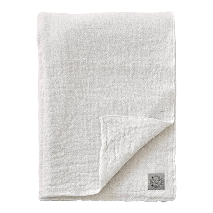 Soft white muslin blanket with a textured, crinkled pattern and a subtle logo patch. Ideal for cozying up.