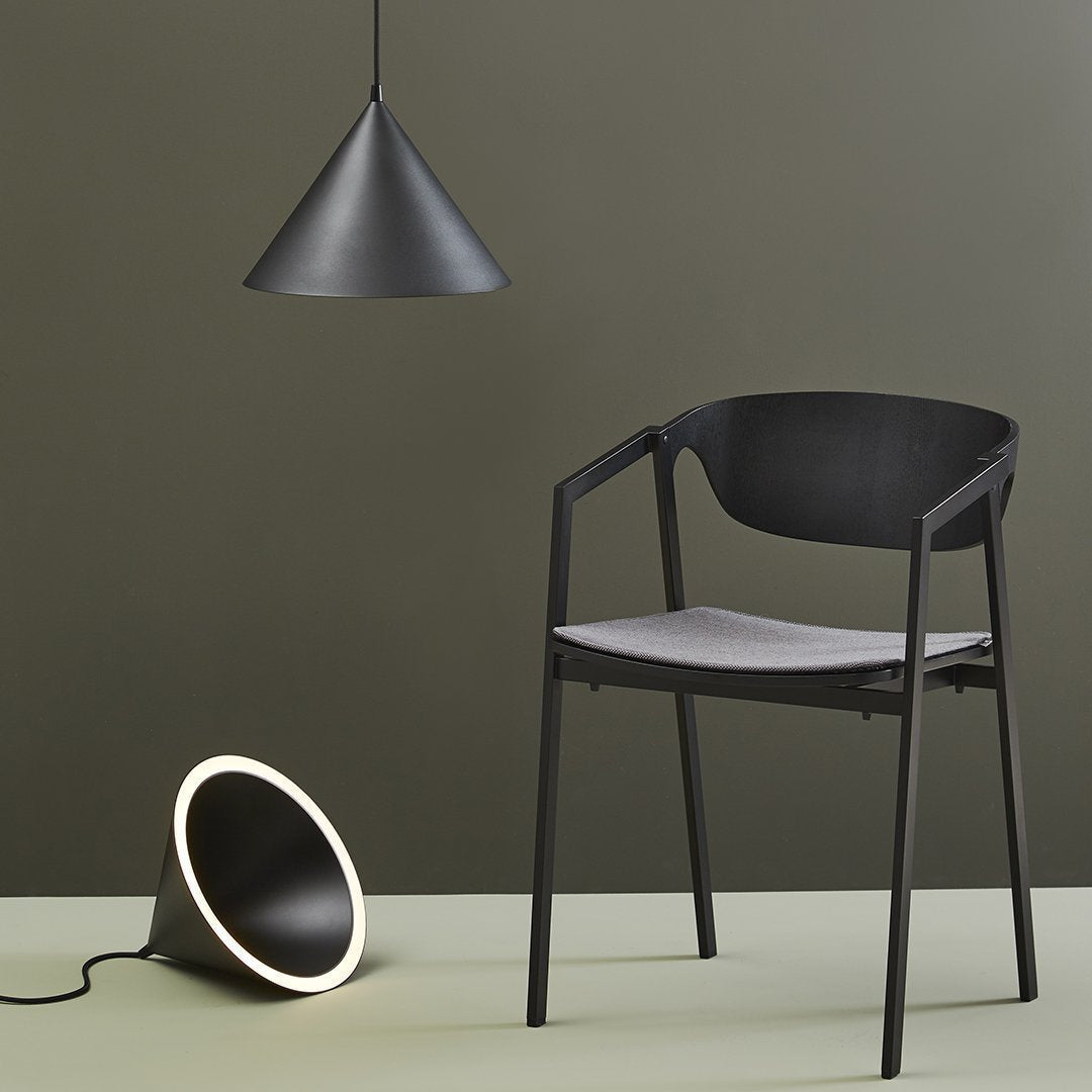 Black chair with gray seat, black pendant lamp, and black cone light on olive green background. Modern minimalist design.