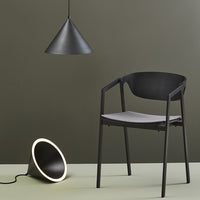 Black chair with gray seat, black pendant lamp, and black cone light on olive green background. Modern minimalist design.
