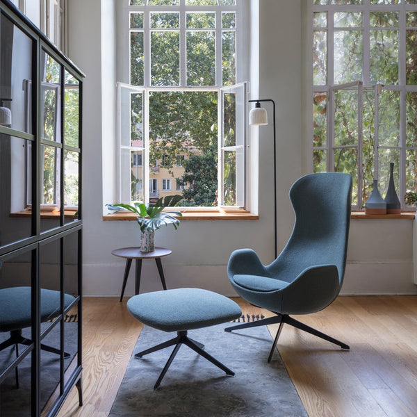 Blue upholstered chair and ottoman set with sleek, modern lines in a bright, airy room with natural light.