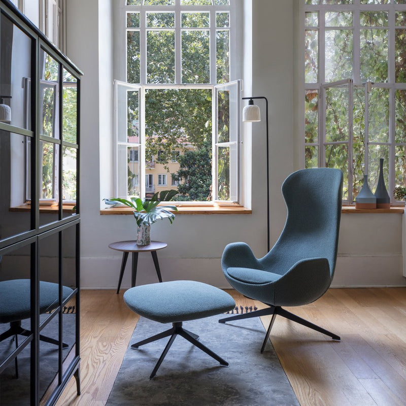 Blue upholstered chair and ottoman set with sleek, modern lines in a bright, airy room with natural light.