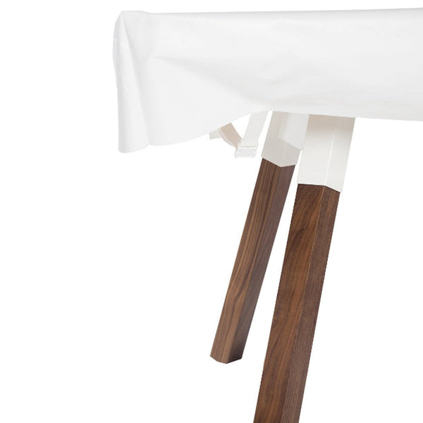 White tablecloth draping over a wooden table with rich brown legs and a sleek, minimalistic design.