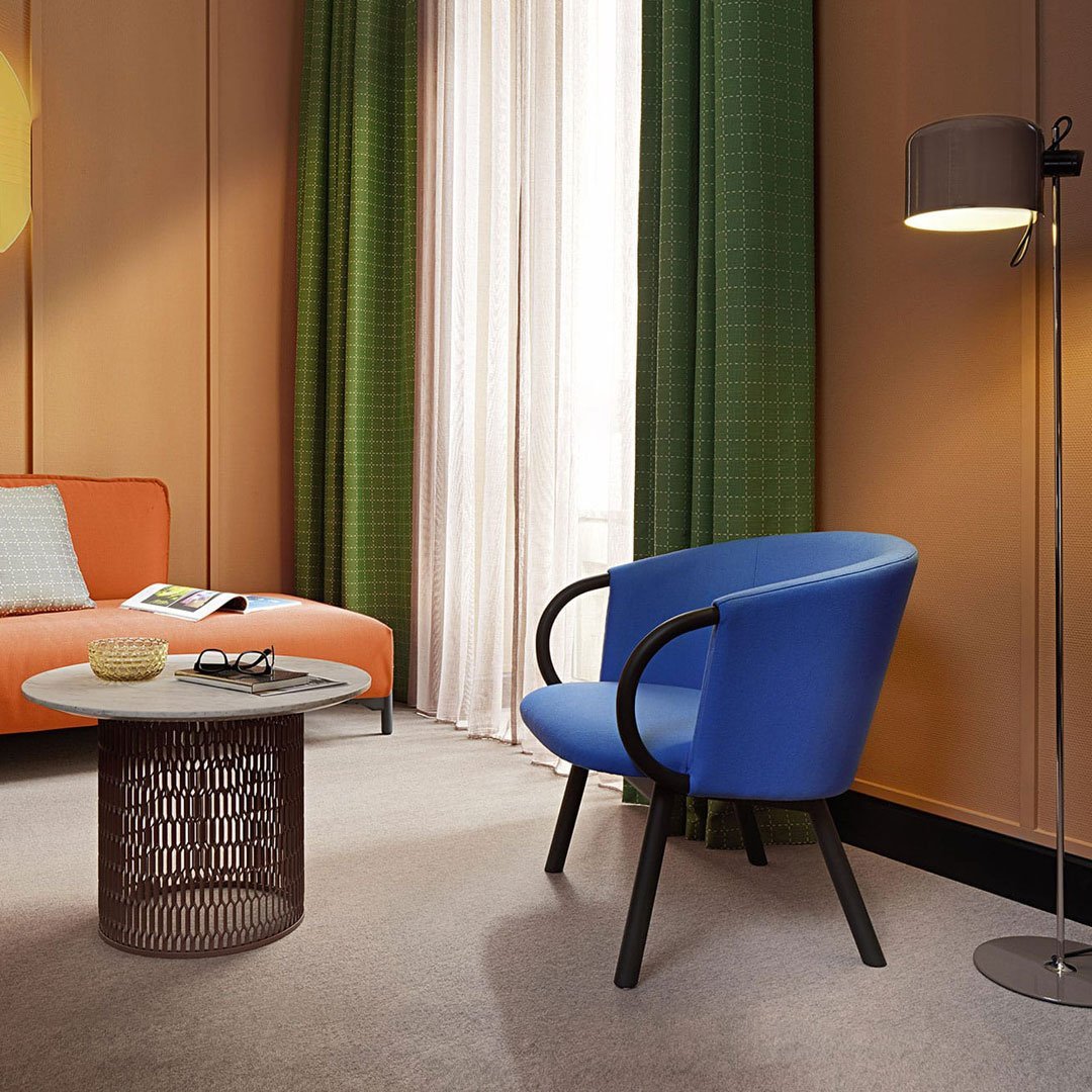 Blue armchair with black legs, orange sofa, green curtains, and a round metal coffee table in a modern room.