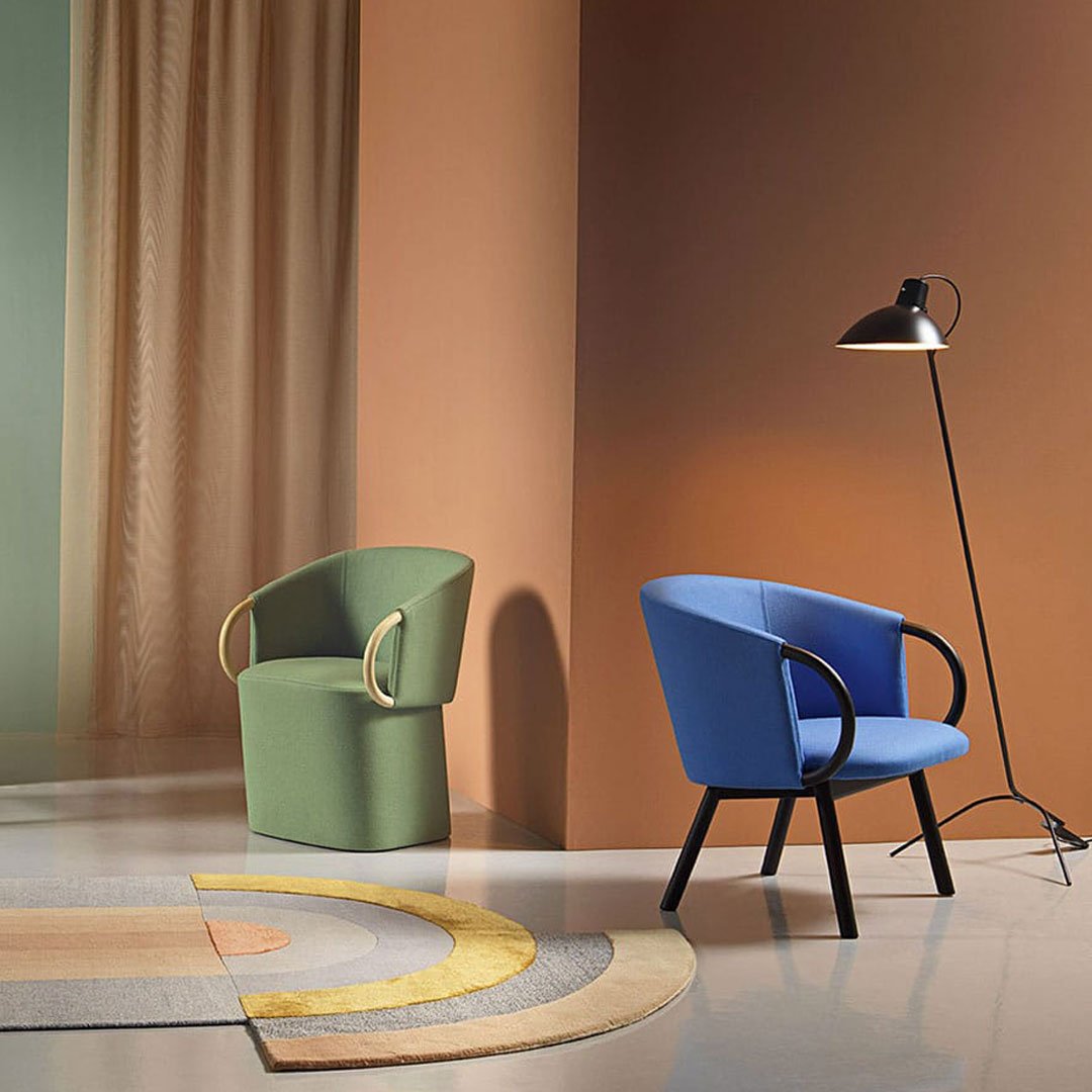 "Green and blue accent chairs with curved designs, set against pastel walls and a geometric patterned rug."