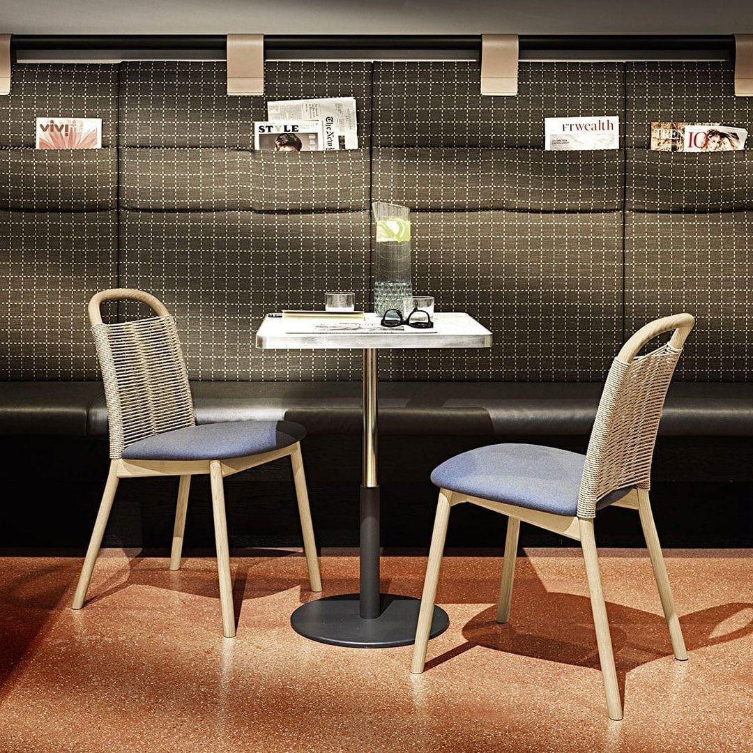 "Modern dining set with light wooden chairs, blue cushions, and a sleek white table against a textured dark wall."