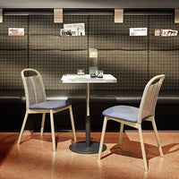 "Modern dining set with light wooden chairs, blue cushions, and a sleek white table against a textured dark wall."