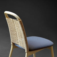 Beige wicker chair with a soft blue upholstery, featuring a sleek, minimalist design against a dark background.
