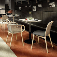 Light cream chairs with woven backs and gray cushions, set against a dark patterned wall and warm terracotta floor.