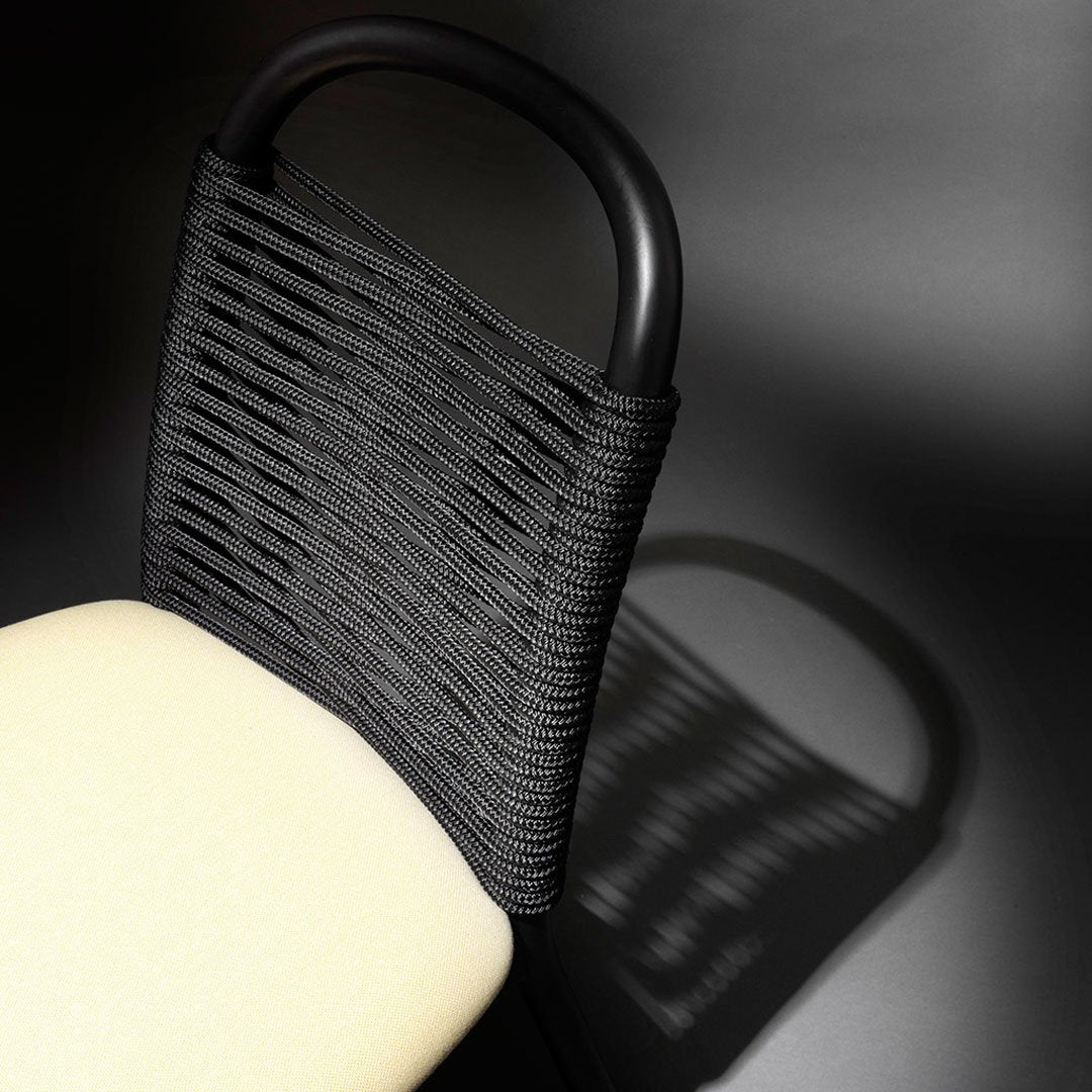 Black woven chair back with cream seat against a dark background, showcasing texture and contrast in design.