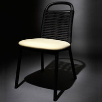 Black woven chair with a cream cushion, featuring a sleek, modern design and geometric patterns. Ideal for minimalistic decor.