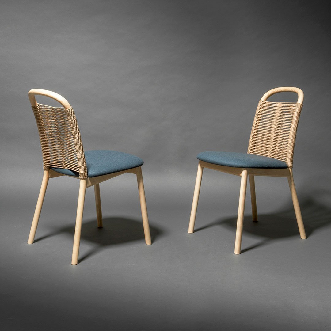 Light wooden chairs with blue cushioned seats and woven backs, set against a dark gray background.