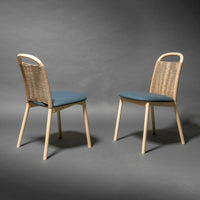 Light wooden chairs with blue cushioned seats and woven backs, set against a dark gray background.