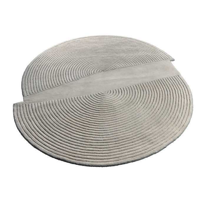 Circular rug featuring soft gray tones with a textured, concentric spiral pattern and a smooth, divided section.