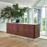 Wooden sideboard in warm walnut finish with a sleek white top and modern metal legs, set against a bright, airy background.