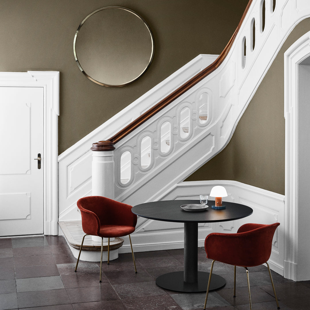 Elegant white staircase and wall with warm olive tones, complemented by bold red chairs and circular mirror accents.