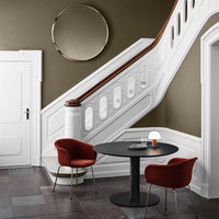 Elegant white staircase and wall with warm olive tones, complemented by bold red chairs and circular mirror accents.