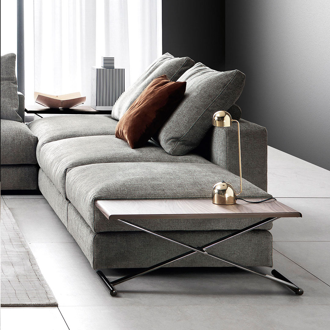Modern gray sofa with soft fabric, complemented by a brown accent pillow and a sleek wooden side table.