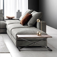 Modern gray sofa with soft fabric, complemented by a brown accent pillow and a sleek wooden side table.