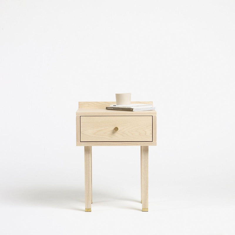 Light wood nightstand with a minimalist design, featuring a simple drawer and natural finish, set against a white background.
