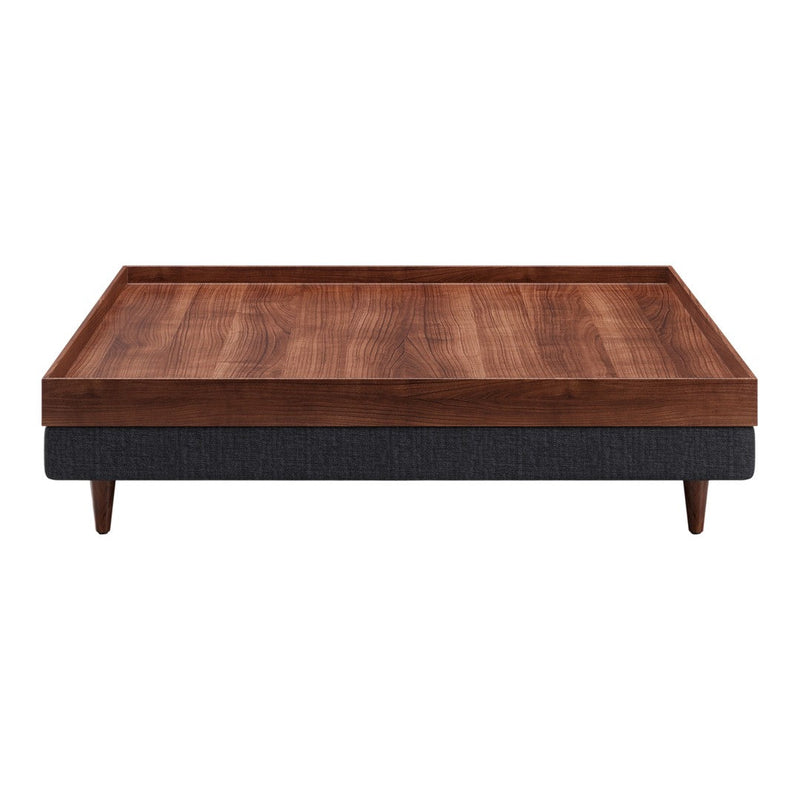 Modern coffee table with a wooden top in warm brown and dark grey fabric base, featuring clean lines and a minimalist design.