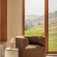 Cozy brown upholstered chair with a smooth round shape, set against a backdrop of natural green hills.
