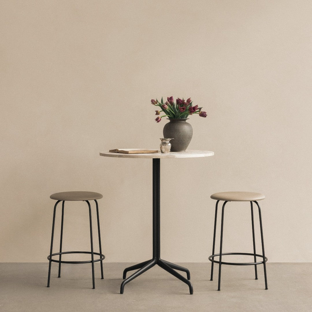 Minimalist round table in white with black base, paired with beige stools, against a soft beige background.