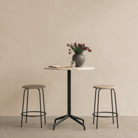 Minimalist round table in white with black base, paired with beige stools, against a soft beige background.