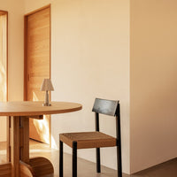 Modern wooden table with a natural finish, paired with a black and woven chair against beige walls.