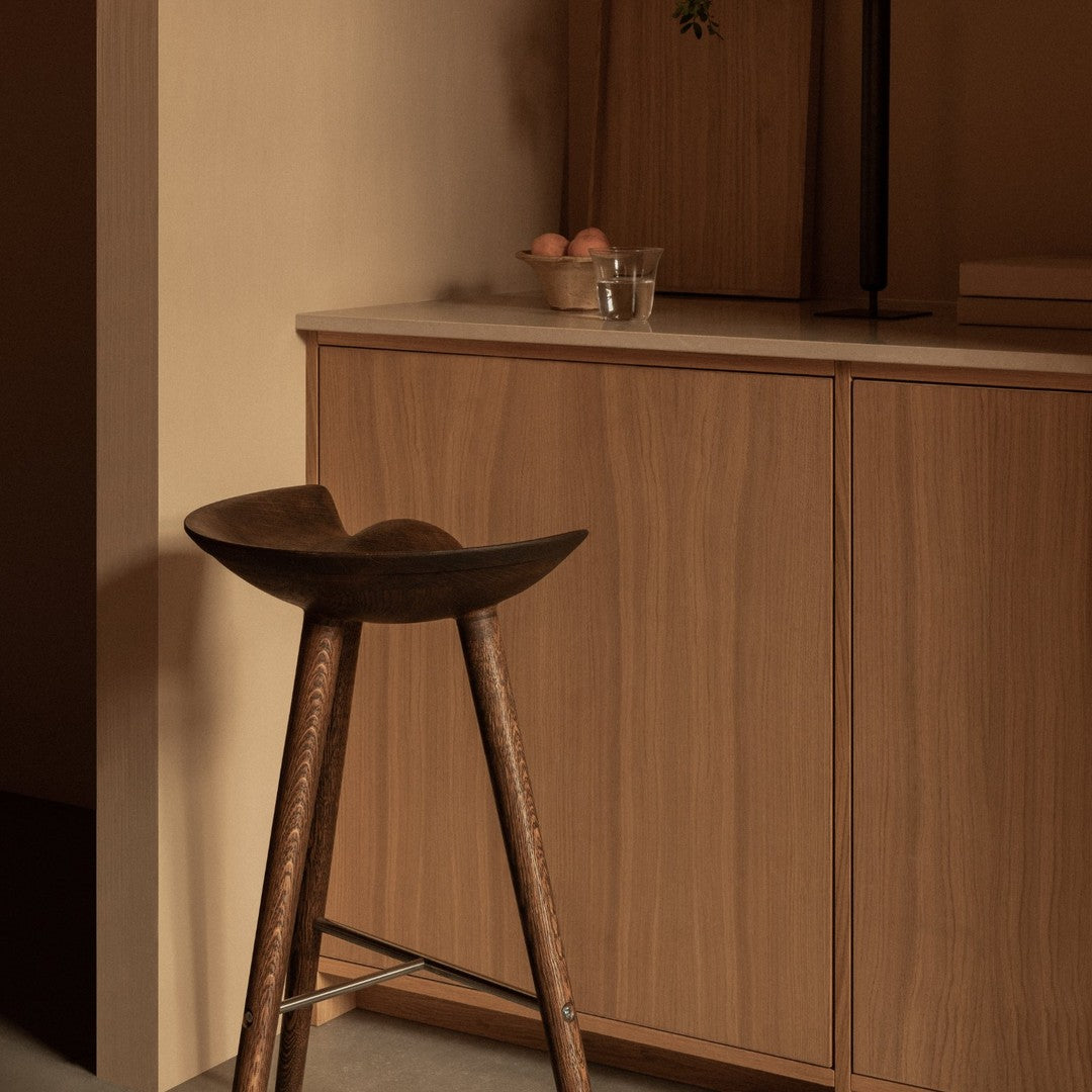 Wooden stool with a curved seat, set against warm beige and brown tones, featuring a minimalist design and smooth textures.