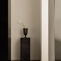 Black vase on a dark marble pedestal against neutral walls, showcasing modern minimalist design and subtle contrasts.