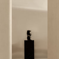 Glossy black sculpture on matte black base, set against a soft beige background. Elegant minimalist design.