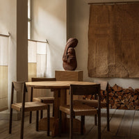 Wooden dining table and chairs with earthy tones, featuring textured wall hangings and a warm, minimalist aesthetic.