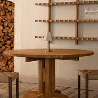 Round wooden dining table with a warm brown finish, featuring a smooth surface and simple design. Neutral tones and natural textures.