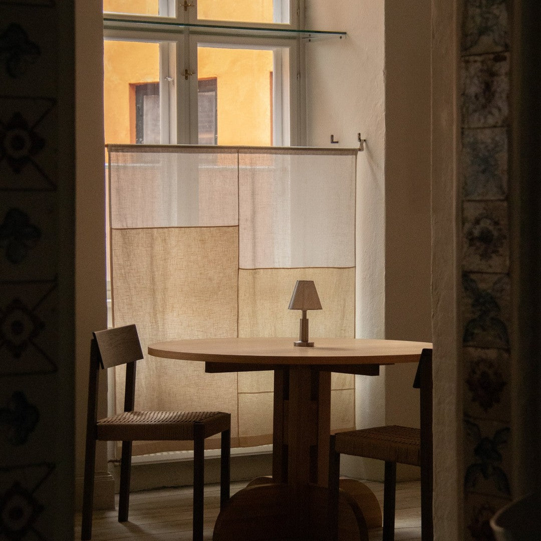 "Neutral-toned fabric curtains with subtle patterns, complementing a warm, natural wood table and chairs."
