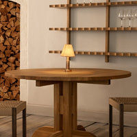 Round wooden table with a natural finish, paired with beige woven chairs and soft yellow lamp accent.