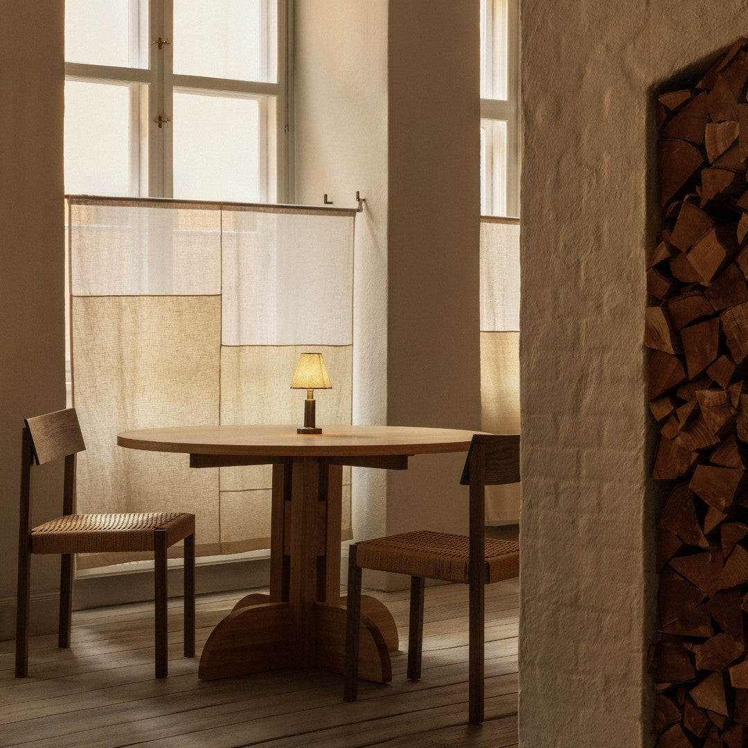 Natural wood table and chairs with soft beige curtains, warm light, and rustic wooden log storage in a cozy interior.