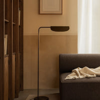 Stylish floor lamp with a sleek black shade, set against warm beige walls and soft gray sofa, featuring a neutral blanket.