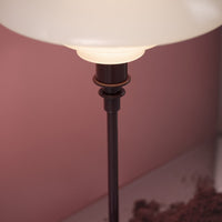 Elegant white lamp shade with a sleek dark metal base, set against a soft pink background. Modern design aesthetics.