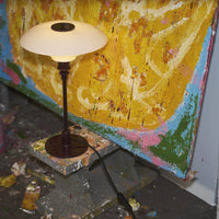 Creamy white lamp on a maroon base, set against a vibrant yellow and pastel blue painted backdrop.
